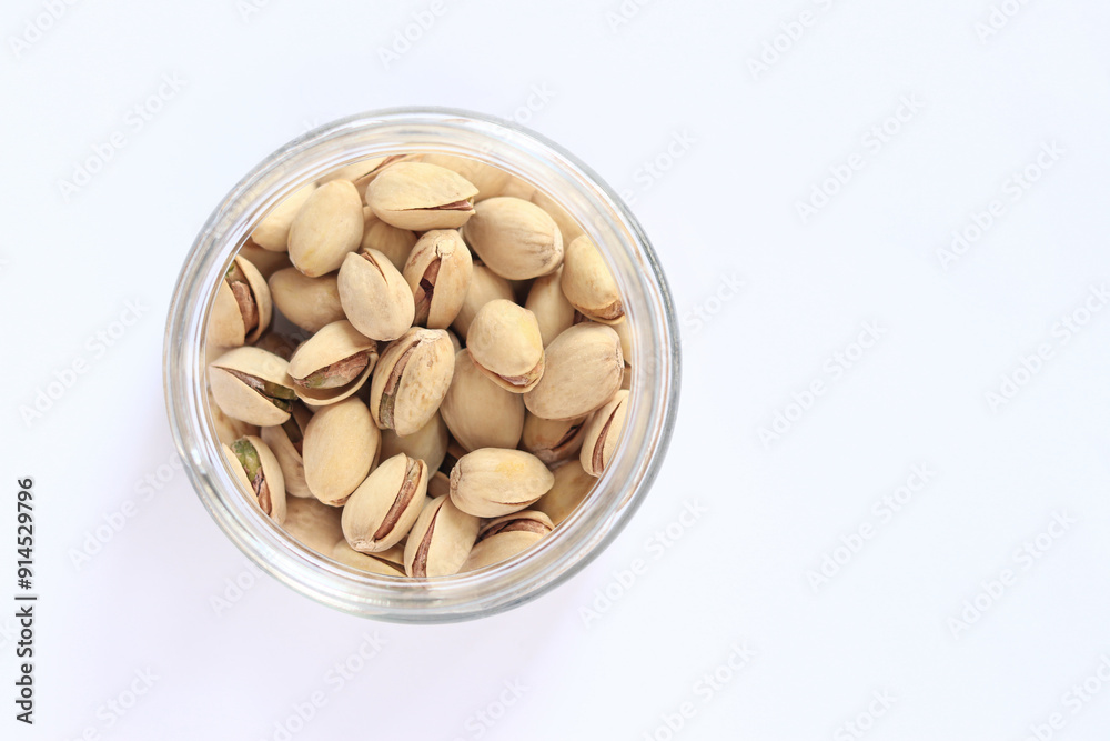 Pistachios in a glass jar on a white background. A handful of dry salted pistachios on a light background, selective focus. Pistachio with shell. Close-up