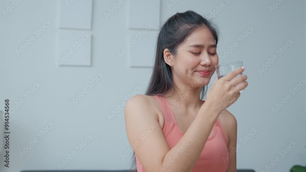 Young woman in fitness attire enjoys a refreshing drink of water in a modern kitchen, showcasing her commitment to a healthy lifestyle Young woman in fitness attire enjoys a refreshing drink of water in a modern kitchen, showcasing her commitment to a healthy lifestyle