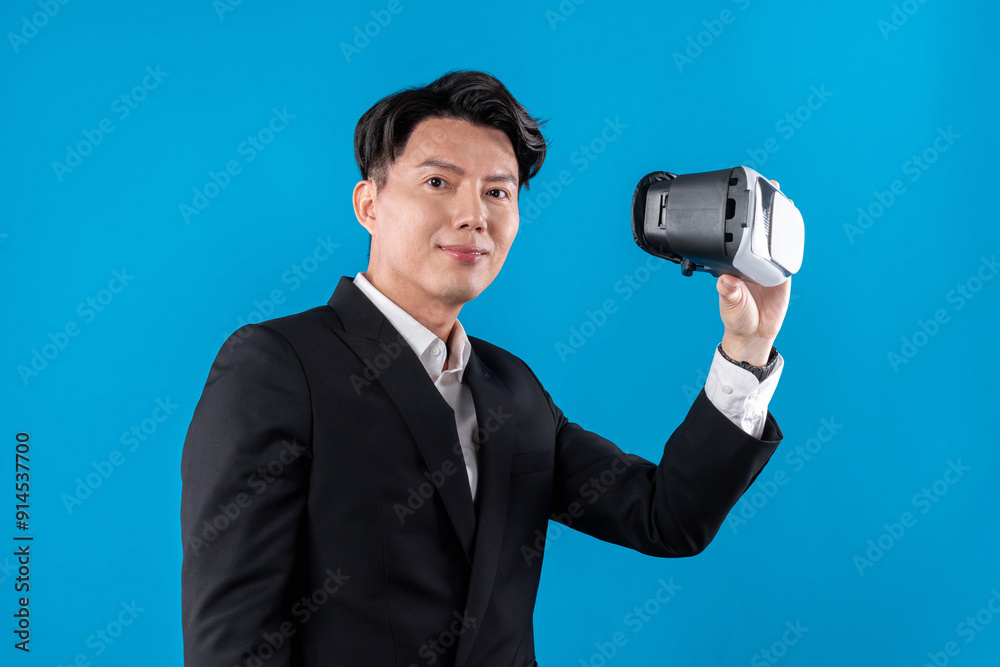 Asian businessman looking at camera holding VR connecting to financial report in futuristic metaverse business data analytics communication technology virtual reality in blue copyspace. Contrivance. Asian businessman looking at camera holding VR connecting to financial report in futuristic metaverse business data analytics communication technology virtual reality in blue copyspace. Contrivance.