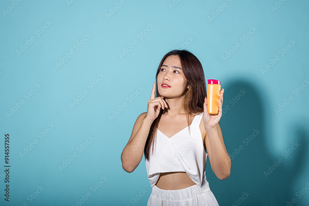Beautiful Asian young woman holding body lotion on hand in studio shot isolated on blue background, Brunette female hold cream sunblock bottle, tube of sunscreen, Beauty cosmetics facial treatment Beautiful Asian young woman holding body lotion on hand in studio shot isolated on blue background, Brunette female hold cream sunblock bottle, tube of sunscreen, Beauty cosmetics facial treatment