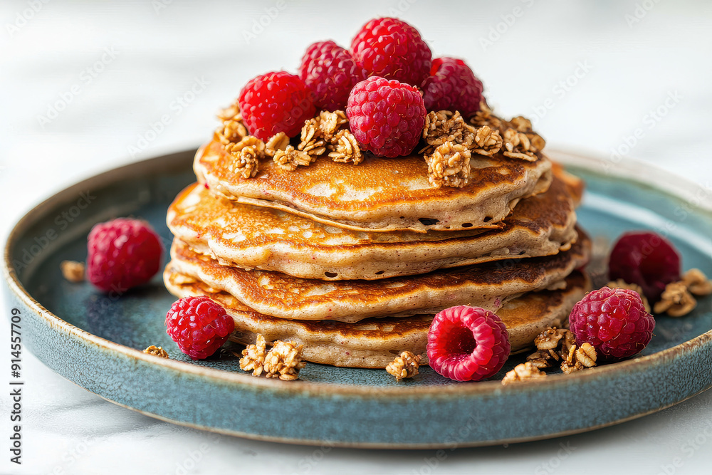 A delightful stack of pancakes topped with juicy raspberries and crunchy granola, beautifully arranged on a blue ceramic plate for an irresistible breakfast treat.