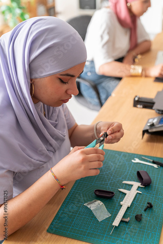 A woman wearing a lavender hijab is seen closely working on assembling small parts in a workshop. The environment is neat and filled with various tools and materials photo