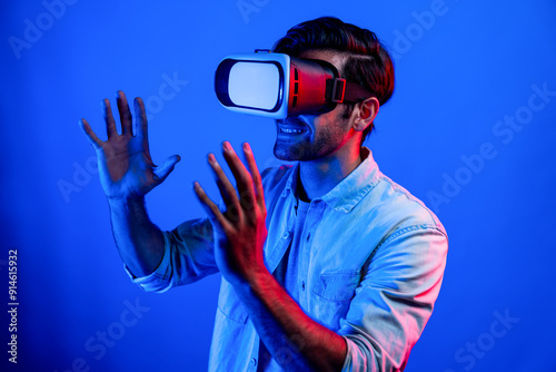 Caucasian smart man holding and moving gesture while using VR goggle. Happy person using headset and goggle while enter virtual world or metaverse with neon light background. Technology. Deviation.