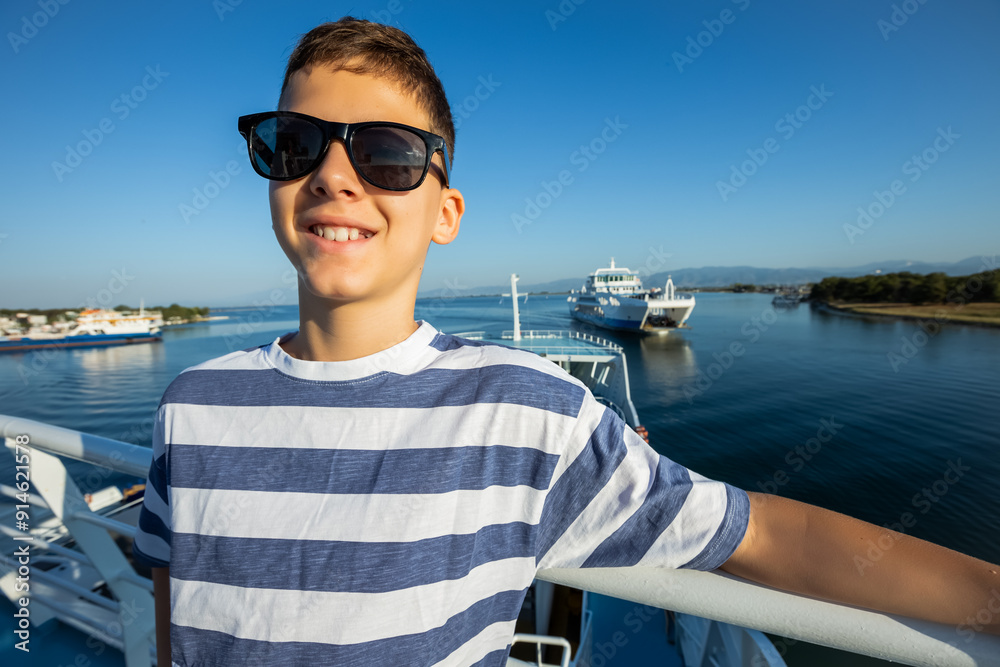 Fototapeta premium A boy, with sunglasses on, surrounded by seagulls rests on a ferry with a beautiful view.