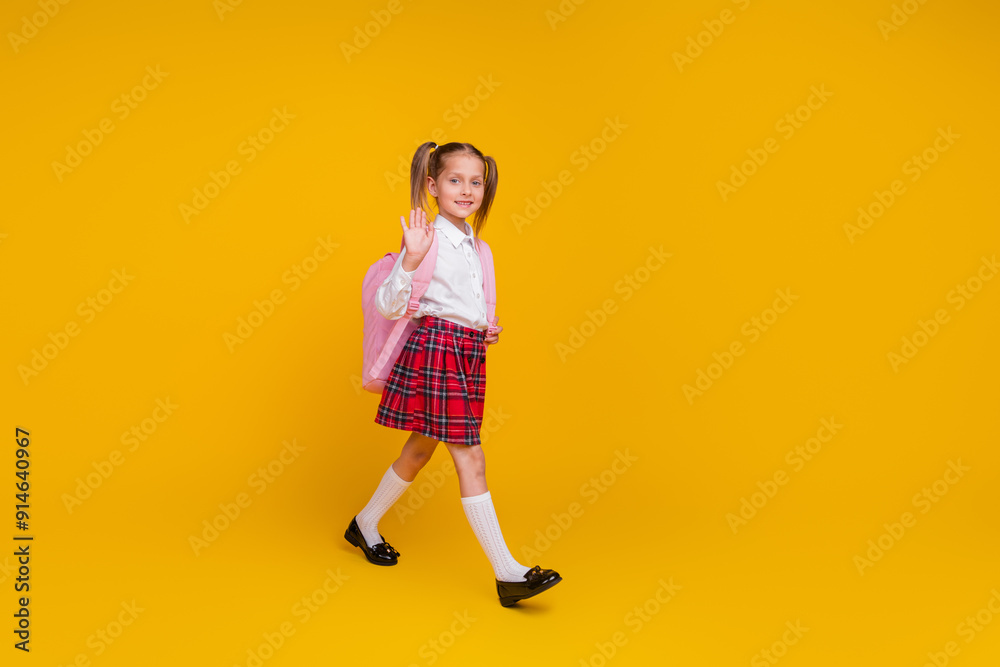 Full body portrait of little schoolkid walk hand wave hi wear uniform isolated on yellow color background Full body portrait of little schoolkid walk hand wave hi wear uniform isolated on yellow color background