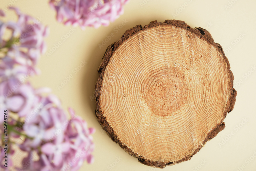 Obraz premium saw cut of a round tree and lilac branches on a beige background, product presentation with lilac