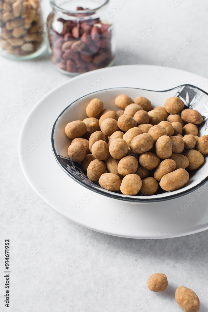 Fried coated peanuts in a white ceramic plate, cracker peanuts on a marble countertop, nigerian peanut snack in a small white plate Fried coated peanuts in a white ceramic plate, cracker peanuts on a marble countertop, nigerian peanut snack in a small white plate