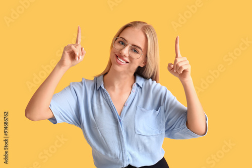 Young thoughtful businesswoman pointing at something on yellow background. Business idea concept