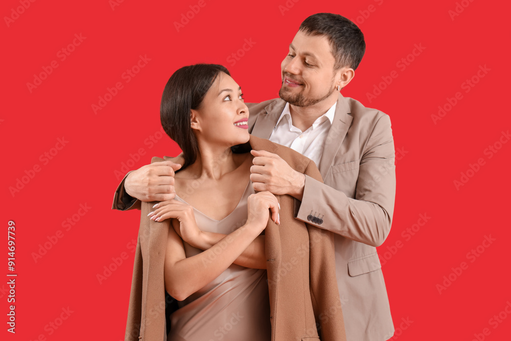 Young man covering his girlfriend with jacket on red background Young man covering his girlfriend with jacket on red background