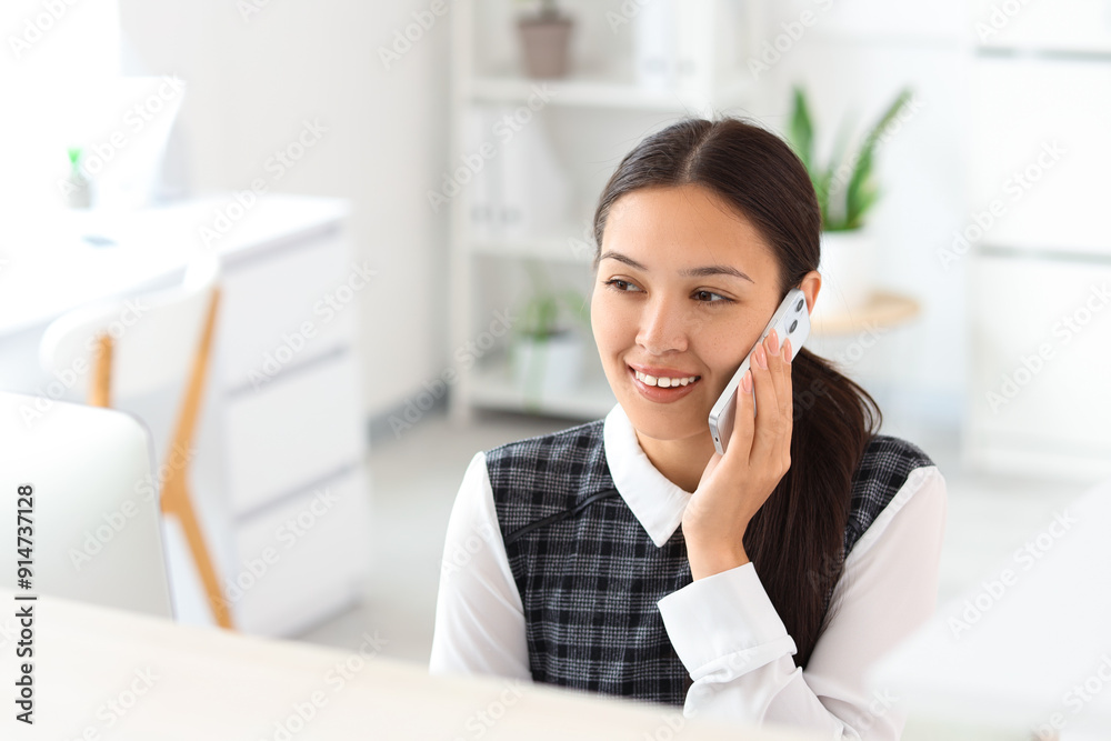 Young female receptionist talking on mobile phone at reception in light office Young female receptionist talking on mobile phone at reception in light office