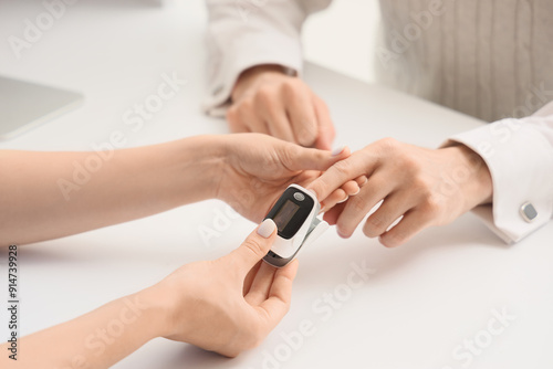 Young man with pulse oximeter and doctor in clinic, closeup