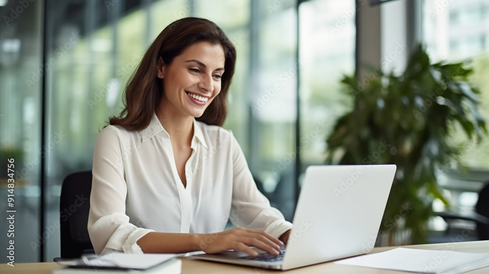 A happy business woman working on her laptop in an office, sitting at her desk with papers and documents around her. A happy business woman working on her laptop in an office, sitting at her desk with papers and documents around her.