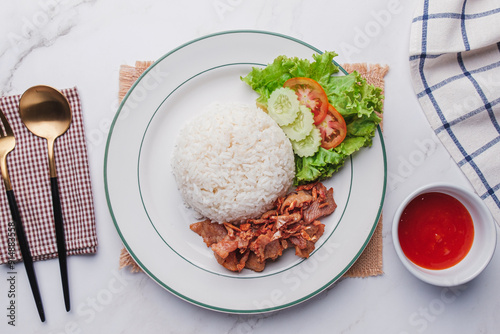 Fried pork with garlic and pepper and cooked jasmine rice with vegetable garnish on blue plate. Easy Thai main meal