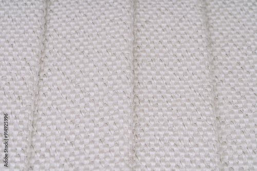 Close-up of white woven fabric with visible metal threads, showing folded sections and intricate texture. The image highlights the weave pattern.