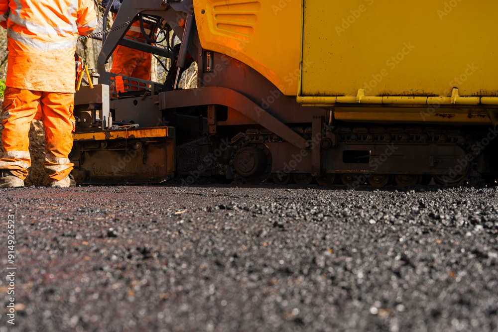 Workers Operating Yellow Asphalt Paver During Road Construction on Sunny Day Workers Operating Yellow Asphalt Paver During Road Construction on Sunny Day