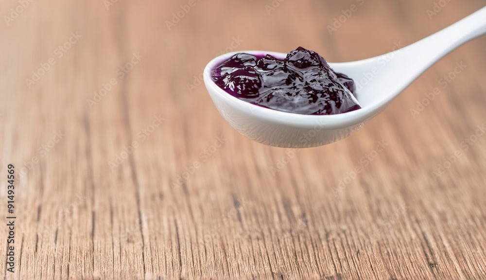White spoon with blueberry jam on wooden table White spoon with blueberry jam on wooden table
