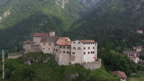 Flight horizontally along the Castle of Stenico at summer. Aerial landscape of Stenico Castle, showcasing the medieval castle and Area naturale Rio Bianco. Castle with Mountains and Clouds photo
