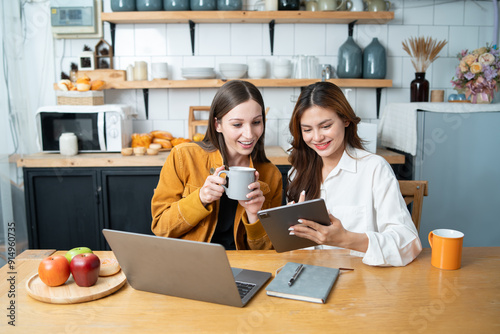 Two women read books, use laptops to work, kitchen