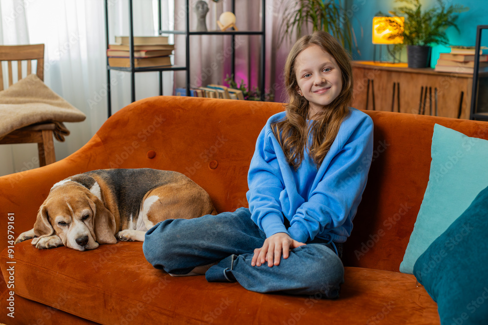 Portrait of smiling young girl with cute beagle dog sitting on orange sofa. Happy preteen female child animal lover spending leisure time with pet dog in living room at home during weekend. Portrait of smiling young girl with cute beagle dog sitting on orange sofa. Happy preteen female child animal lover spending leisure time with pet dog in living room at home during weekend.