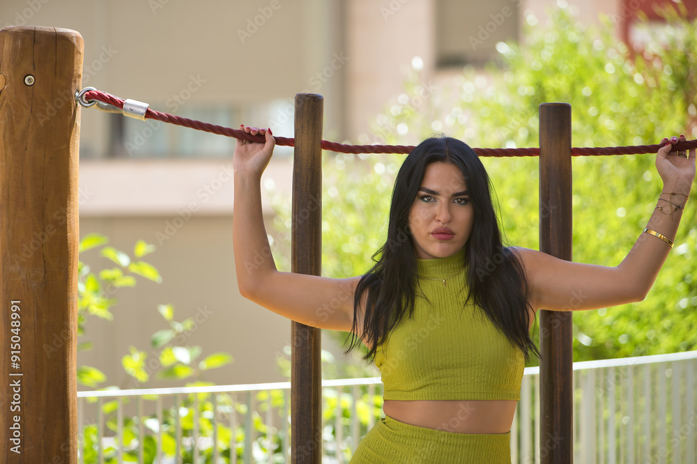 Fototapeta premium Young, beautiful, brunette, latina woman, wearing a green suit, with a sensual and provocative look while holding a rope with her hands. Concept beauty, fashion, trend, city.