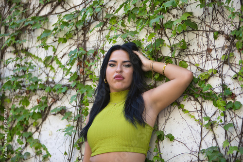 Portrait of young, beautiful, brunette, Latina woman, wearing a green suit, with tender and delicate look, leaning against a wall with a background of ivy. Concept beauty, fashion, trend, city. photo