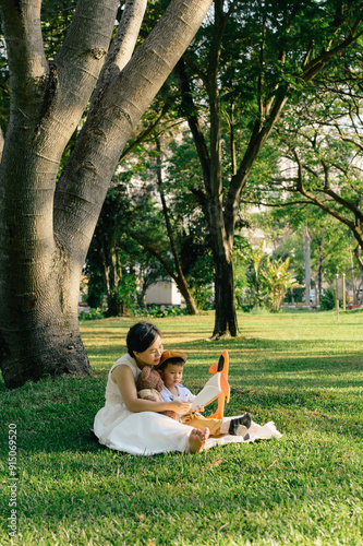 Asian mother reading fairy tales for her son under the tree in the park 