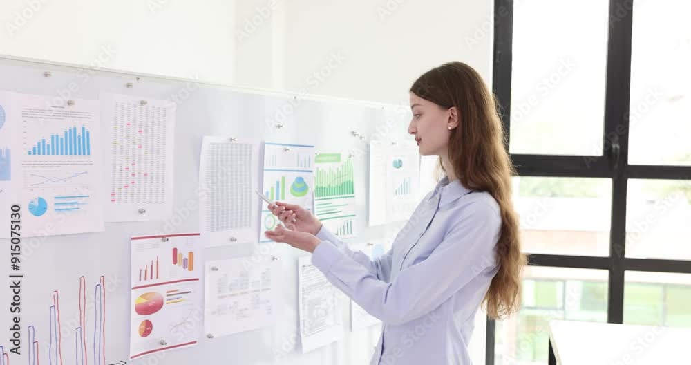 Young businesswoman explains graphs and pie charts attached to whiteboard. Professional employee explains nuances of important reports at presentation Young businesswoman explains graphs and pie charts attached to whiteboard. Professional employee explains nuances of important reports at presentation
