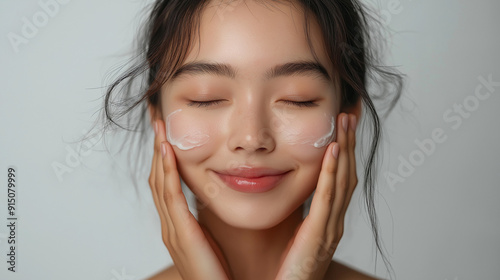 Korean Woman applying skincare product to her face with a relaxed expression in a bright, minimalistic setting