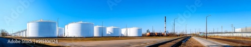 Sustainable Industrial Power: Towering White Storage Tanks by the Roadside and Railway, Set Against a Pristine Blue Sky