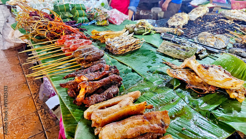 Assorted grilled meats, sausages, and fish displayed on banana leaves at a market