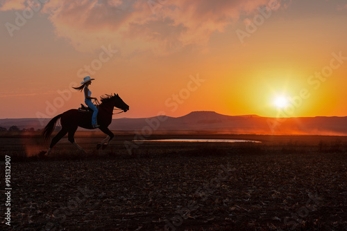 silhouette cowgirl in the sunset riding galloping in the prairie near a waterhole