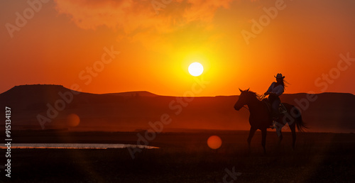 Obraz na płótnie silhouette cowgirl in the sunset riding in the prairie near a waterhole
