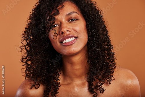 Young black woman with bare shoulders and curly black hair, smiling against an orange background photo