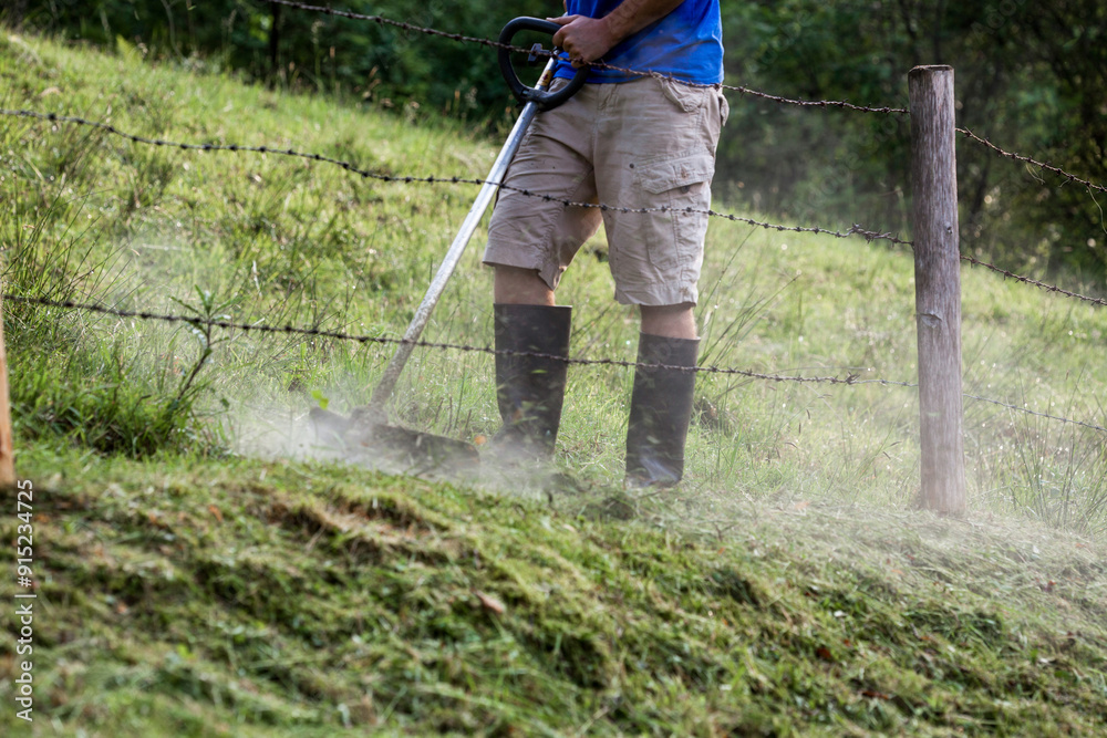 man in rubber boots mowing the grass with a lawn trimmer