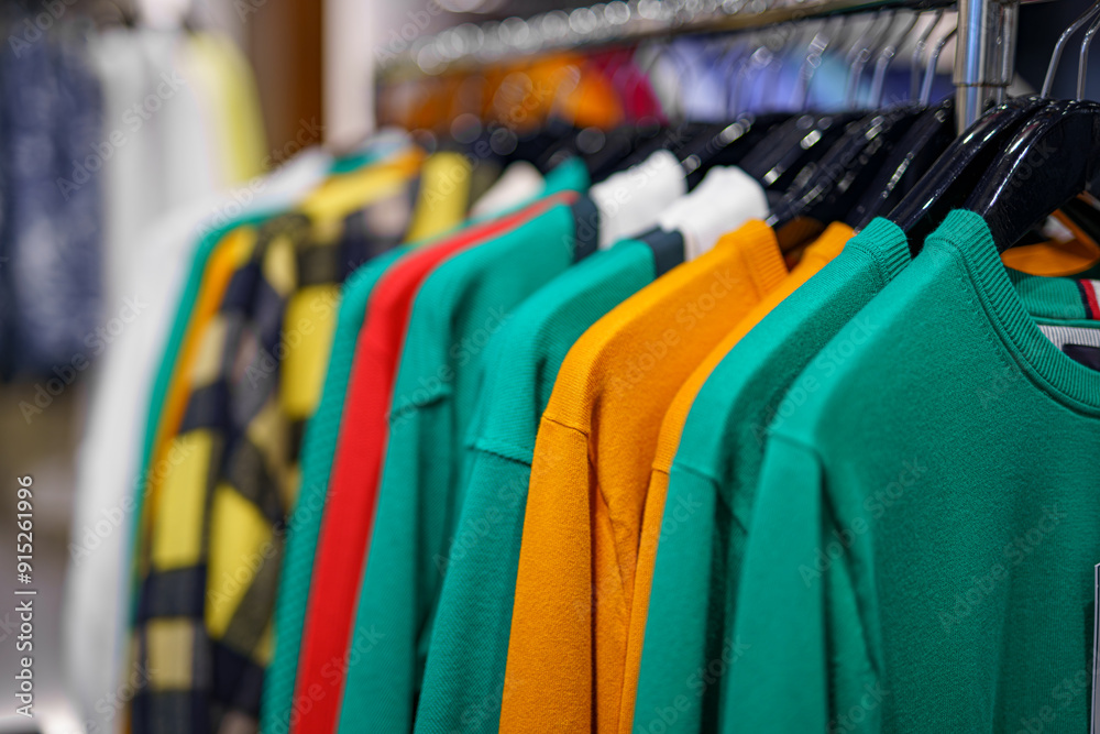 Sweaters and T-shirts of different colors on a hanger for sale in a shopping mall.