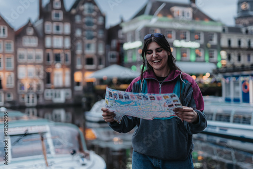 Canvas Print Young girl happily exploring Amsterdam by the canal, holding a map and enjoying the city ambiance on a pleasant evening