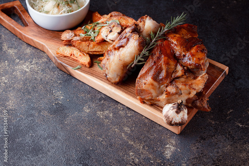 A set dish: a large fried piece of meat on the bone, country-style grilled potatoes, a mini salad of cabbage, bean sprouts, chia seeds and green onions. Original serving on a wooden cutting board. photo