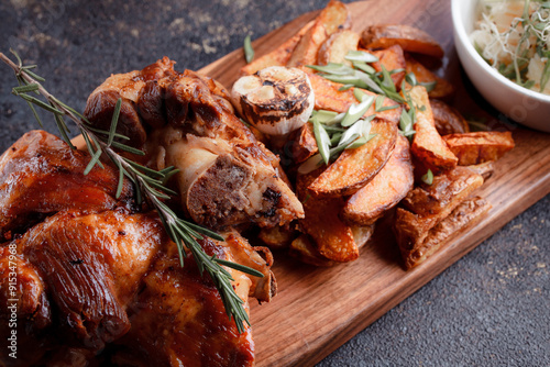 A set dish: a large fried piece of meat on the bone, country-style grilled potatoes, a mini salad of cabbage, bean sprouts, chia seeds and green onions. Original serving on a wooden cutting board. photo