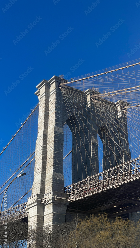 Fototapeta premium Massiver Pfeiler der Brooklyn Bridge mit Stahlseilen und blauem Hintergrund