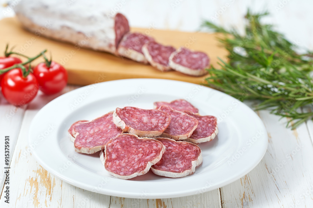 traditional Spanish salami fuet sausage or dry sausage cut in slices on a white ceramic plate, isolated on a kitchen table. traditional Spanish salami fuet sausage or dry sausage cut in slices on a white ceramic plate, isolated on a kitchen table.