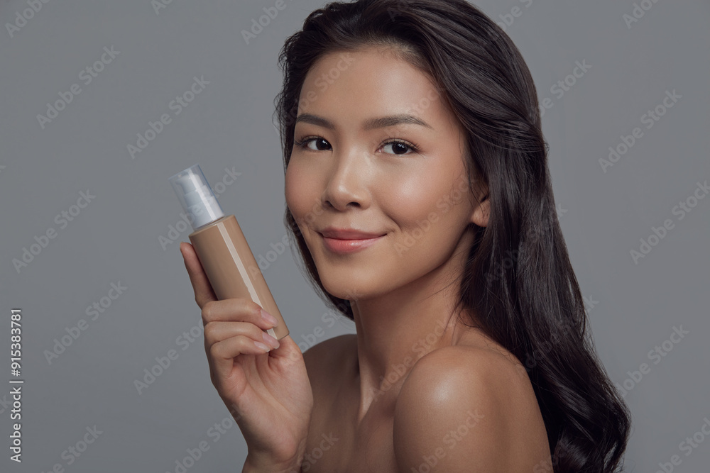 asian woman holding cosmetic tube for beauty procedures on a grey isolated background asian woman holding cosmetic tube for beauty procedures on a grey isolated background