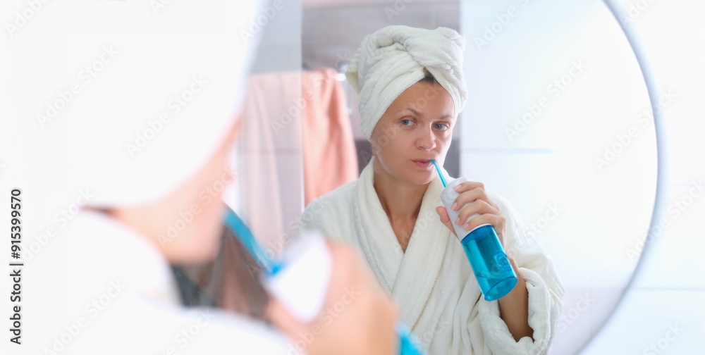 A woman in a dressing gown with a towel on her head is brushing her teeth with an irrigator. Oral hygiene, beauty and health A woman in a dressing gown with a towel on her head is brushing her teeth with an irrigator. Oral hygiene, beauty and health