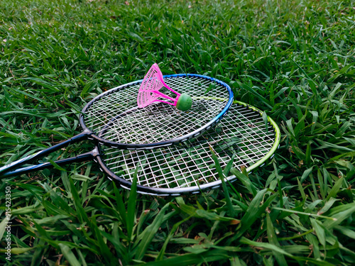Closeup side view of two badminton rackets and shuttlecock on green grass