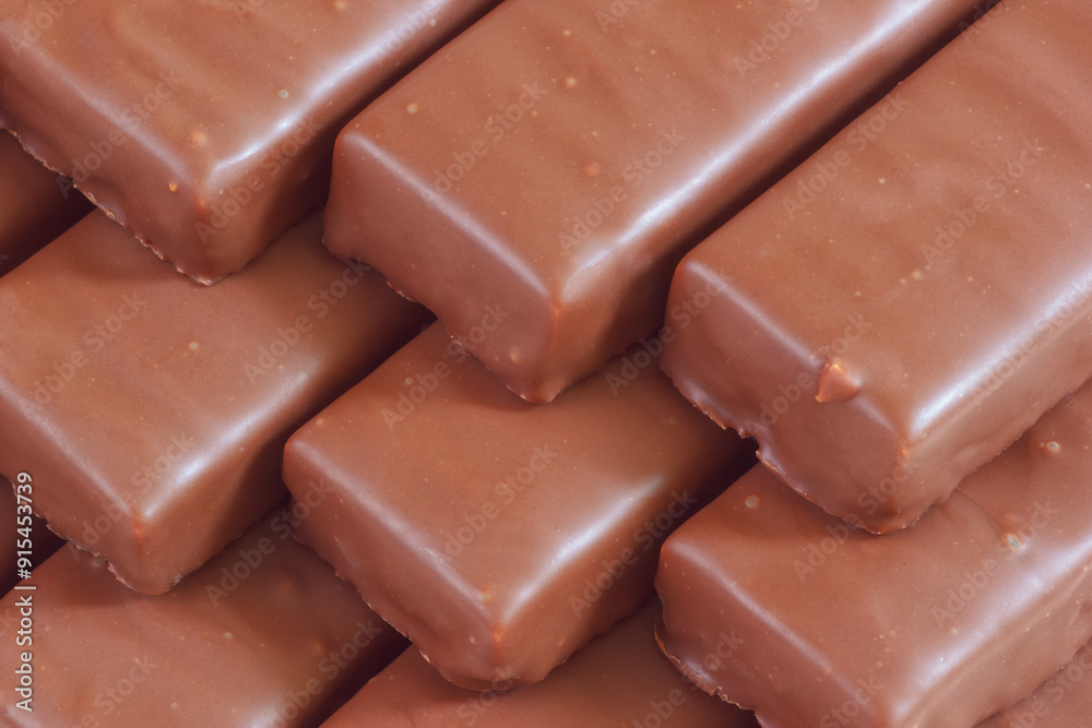 The rows of chocolate bars. The sweet dessert confectionery with brown glaze. The yummy food with a lot of calories. Closeup view. The rows of chocolate bars. The sweet dessert confectionery with brown glaze. The yummy food with a lot of calories. Closeup view.