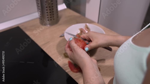 Unrecognizable Young Woman Peeling a Tomato with a Knife to Prepare a Fresh Salad in the Kitchen photo