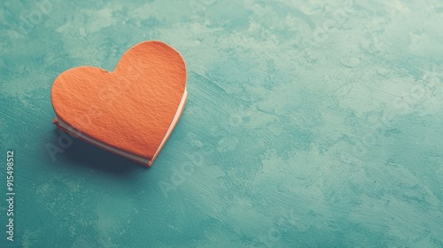 orange wooden heart placed on a textured turquoise surface, symbolizing love and affection.