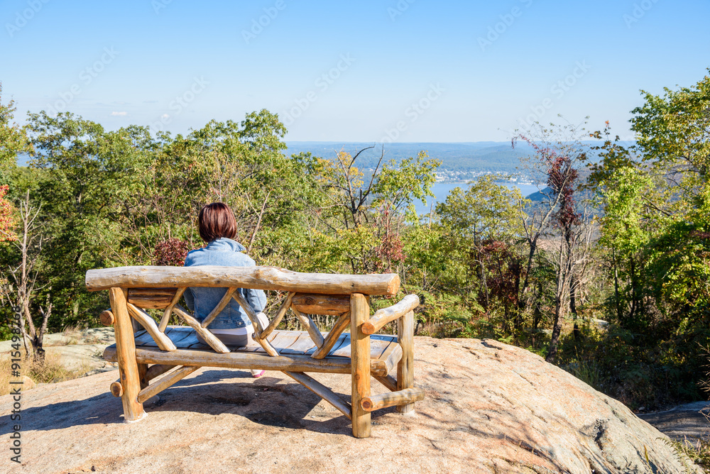 Woman tourist looking at a magnificent view while sitting alone on a wooden bench on the top of a mountain on a sunny autumn day Woman tourist looking at a magnificent view while sitting alone on a wooden bench on the top of a mountain on a sunny autumn day