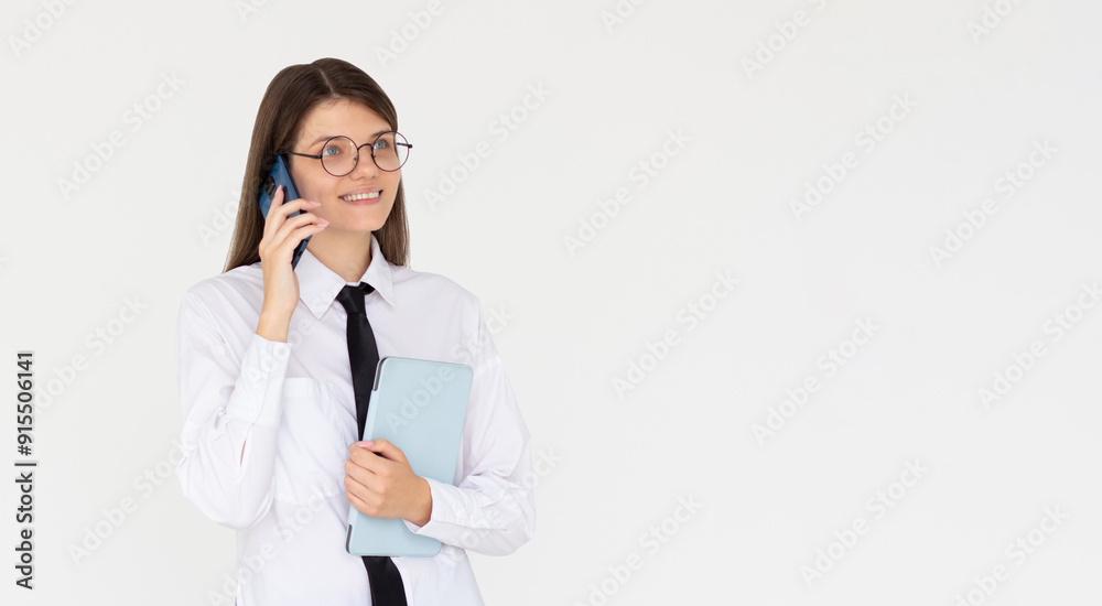 Joyful european woman in white shirt is speaking on the phone with classmates friends while smiling preparing to go to University High school holding tablet in hand. Joyful european woman in white shirt is speaking on the phone with classmates friends while smiling preparing to go to University High school holding tablet in hand.