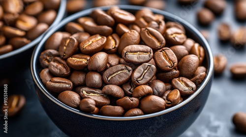 Close-up of a bowl filled with roasted coffee beans placed on a dark surface with additional coffee beans in the background.