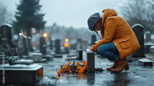 Woman grieving at a cemetery in winter, kneeling by a tombstone with orange flowers on the ground under a gray, raining sky.